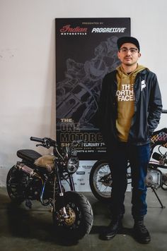 a man standing next to a motorcycle in front of a poster