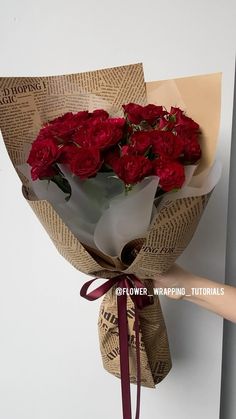 a bouquet of red roses wrapped in burlock and tied to a white wall