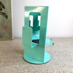 a green book stand sitting on top of a carpeted floor next to a painting