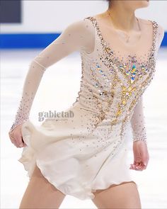 a female figure skating in a short white dress