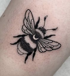 a small black and white tattoo of a bee on the right side of the leg