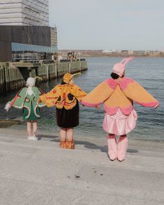 three people dressed in costumes walking along the water's edge with their arms around each other