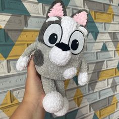 a hand holding a small stuffed animal in front of a wall