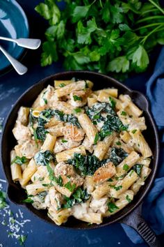 a skillet filled with pasta and spinach on top of a blue tablecloth