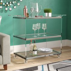 a bar cart with wine glasses and plates on it in front of a green wall