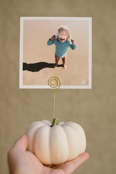 a hand holding a small white pumpkin with a photo on it's stick in the middle