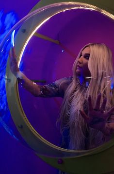 a woman with long blonde hair standing in front of a circular mirror holding her hand up