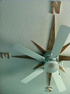 a white ceiling fan with wooden blades hanging from it's center and two letters on the wall