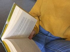 a person sitting down reading a book with their hands on the back of his lap