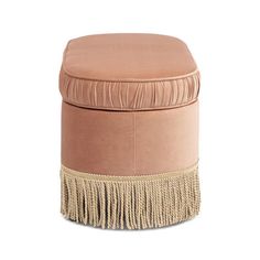 a pink ottoman with fringe trim on the top and bottom, sitting in front of a white background