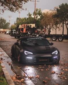 a black sports car parked on the side of a road next to a dump truck