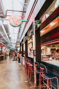 the inside of a restaurant with red chairs and people walking around it in front of the counter