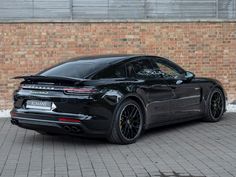 a black porsche panamera parked in front of a brick wall