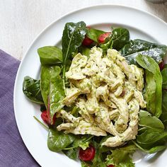 a white plate topped with spinach and chicken salad on top of a purple cloth