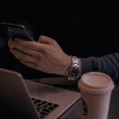 a person sitting at a table with a laptop and cell phone in their hands, while holding a coffee cup