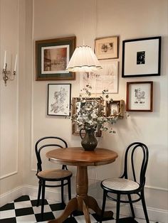 a dining room table with chairs and pictures on the wall above it, in front of a black and white checkered floor