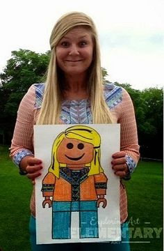 a woman holding up a drawing of a girl with blonde hair and blue pants in front of green grass