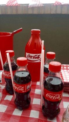 coca - cola bottles are lined up on a checkered tablecloth with utensils