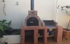 an outdoor brick pizza oven with potted plants on the side and windows in the back