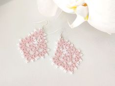 a pair of pink and white beaded earrings on top of a table next to a flower