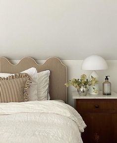 a bed with white sheets and pillows next to a night stand on a wooden dresser