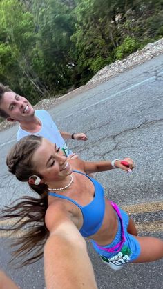 two people are running in the street with trees in the background and one person is smiling at the camera