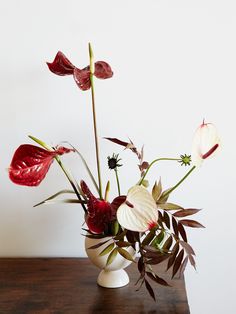 a vase filled with red and white flowers on top of a wooden table next to a wall