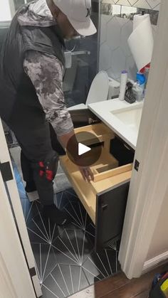 a man in grey jacket and white hat standing next to a sink with an open drawer