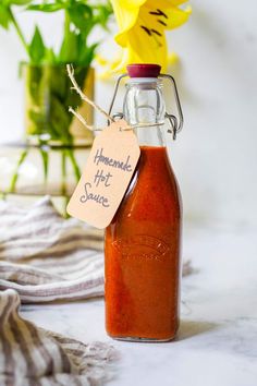 a jar filled with sauce sitting on top of a table next to a yellow flower