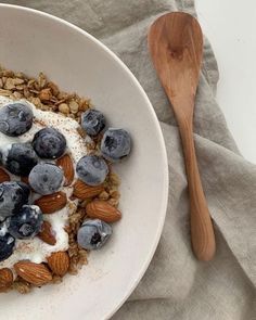 a bowl filled with granola, blueberries and almonds next to a wooden spoon