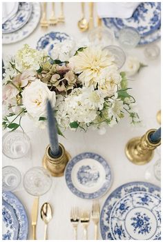 the table is set with blue and white plates, silverware, and floral centerpieces