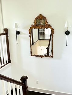 an ornate mirror hanging on the wall above a stair case in a home with white walls and wood floors