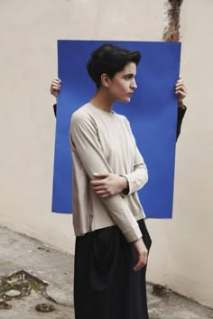 a woman standing in front of a blue piece of paper with her hands on her hips