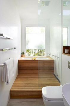 modern bathroom with wooden steps leading up to the bathtub and shower area, along with a white toilet and sink