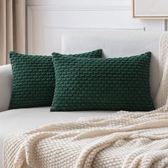 two green knitted pillows sitting on top of a couch next to a white blanket