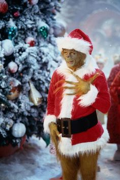 a monkey dressed as santa claus standing in front of a christmas tree with his hands on his chest