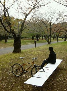 a person sitting on a bench with a bike parked next to it in the park