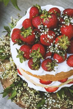 a white cake with strawberries on top and flowers around the edges is surrounded by greenery