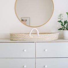 a basket on top of a dresser next to a mirror and potted green plant