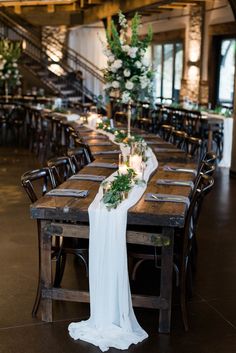 a long table with candles and greenery is set up in the middle of an empty room