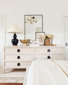 a bedroom with white furniture and pictures on the wall, including an antique chest of drawers