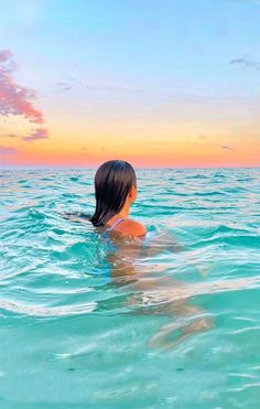 a woman is swimming in the ocean with her back to the camera and looking at the sky