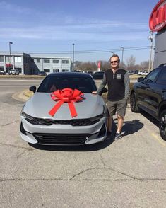 a man standing next to a gray car with a red bow on it's hood