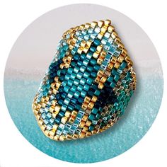 a blue and gold beaded ring sitting on top of a white circle with water in the background