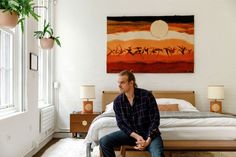 a man sitting on top of a wooden bed in a bedroom next to a window