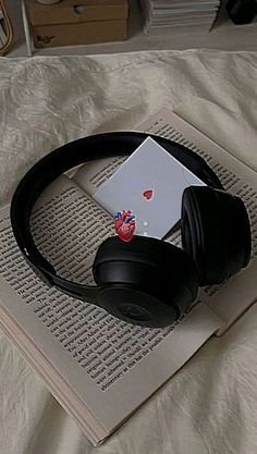 an open book with headphones and a laptop on it sitting on top of a bed