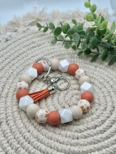 an orange and white beaded bracelet with tassels on a table next to a plant