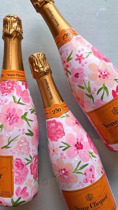 three champagne bottles with pink flowers and gold foil wrappers on them, lined up next to each other