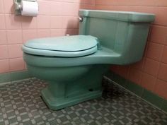 a green toilet sitting in a bathroom next to a pink tiled wall with a roll of toilet paper on it