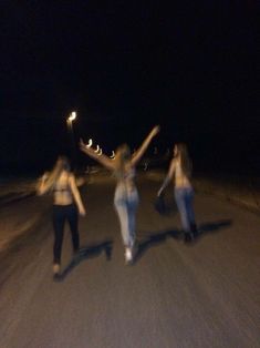 three women standing on the side of a road at night with their arms in the air